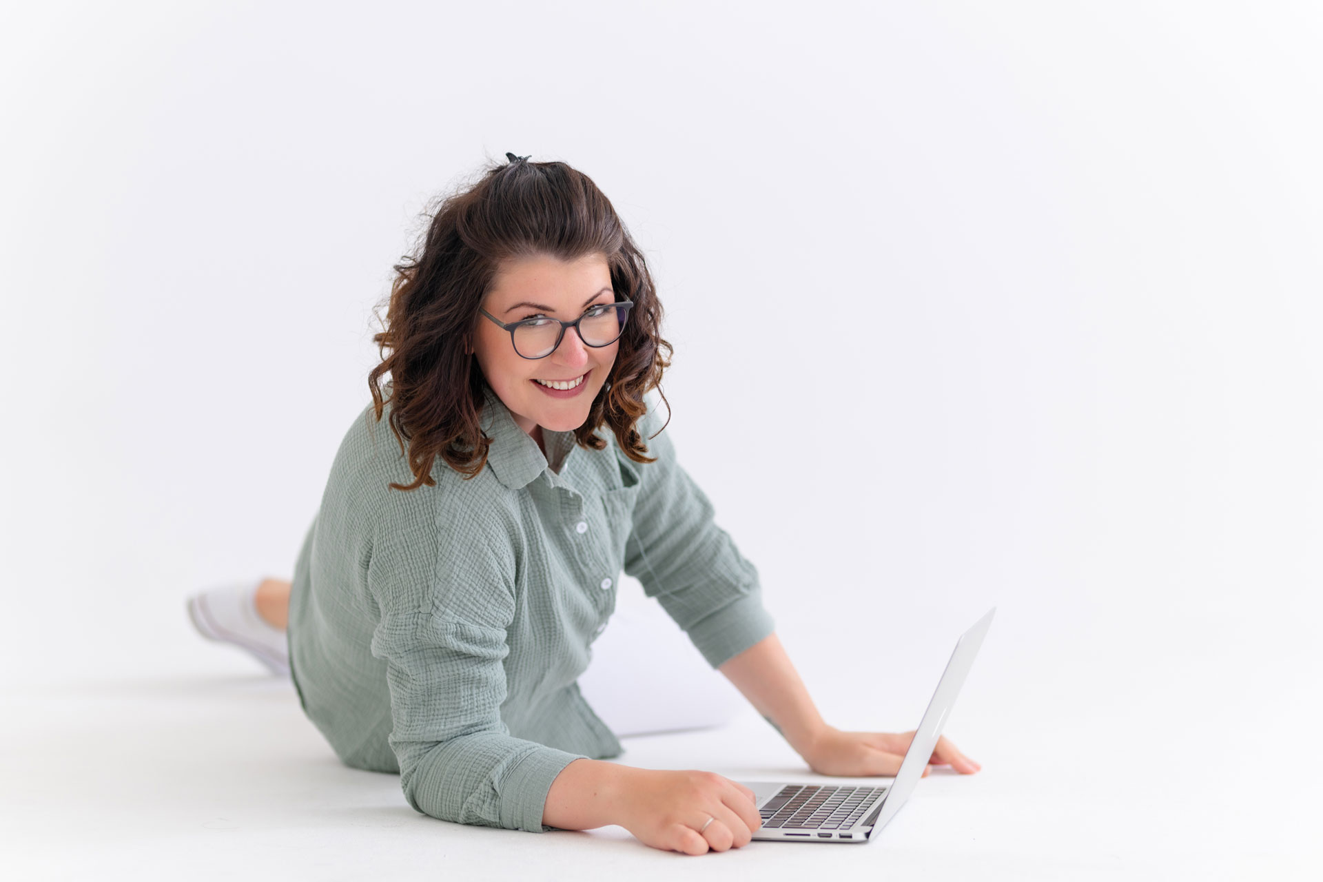 Evi liegt auf dem Boden und arbeitet lachend am Laptop
