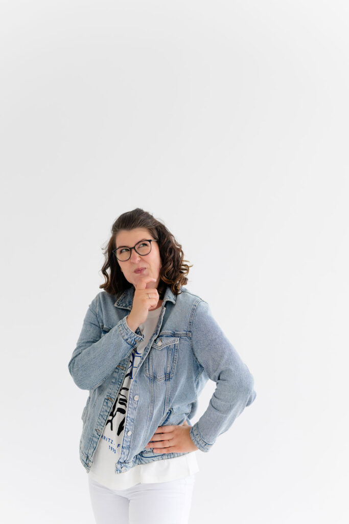 Evi in Jeansjacke, nachdenklich mit der Hand am Kinn