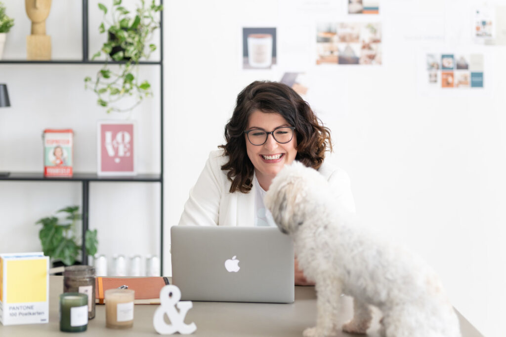 Evi am Schreibtisch mit Laptop, ihr Hund schaut ihr über die Schulter