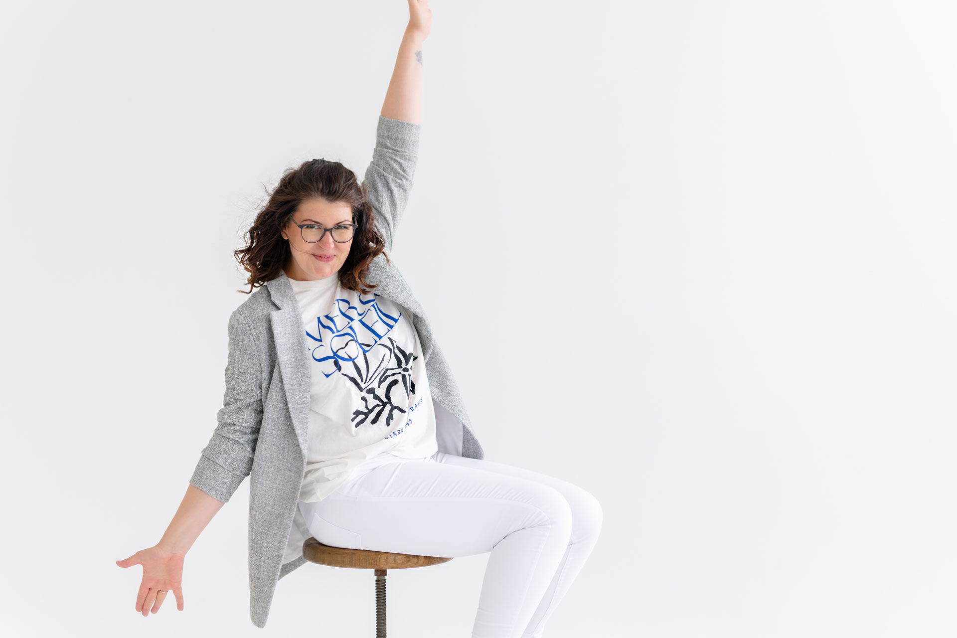 Evi sitzt auf einem Hocker und reckt fröhlich den Arm in die Luft