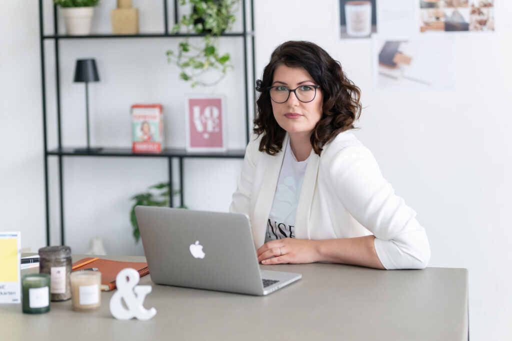 Evi sitzt lächelnd am Schreibtisch vor ihrem Laptop