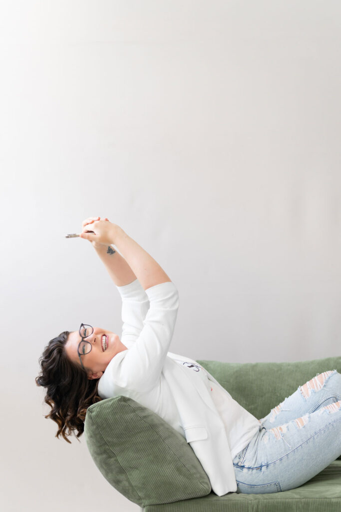 Evi liegt lachend auf einem grünen Sofa und streckt die Arme in die Luft