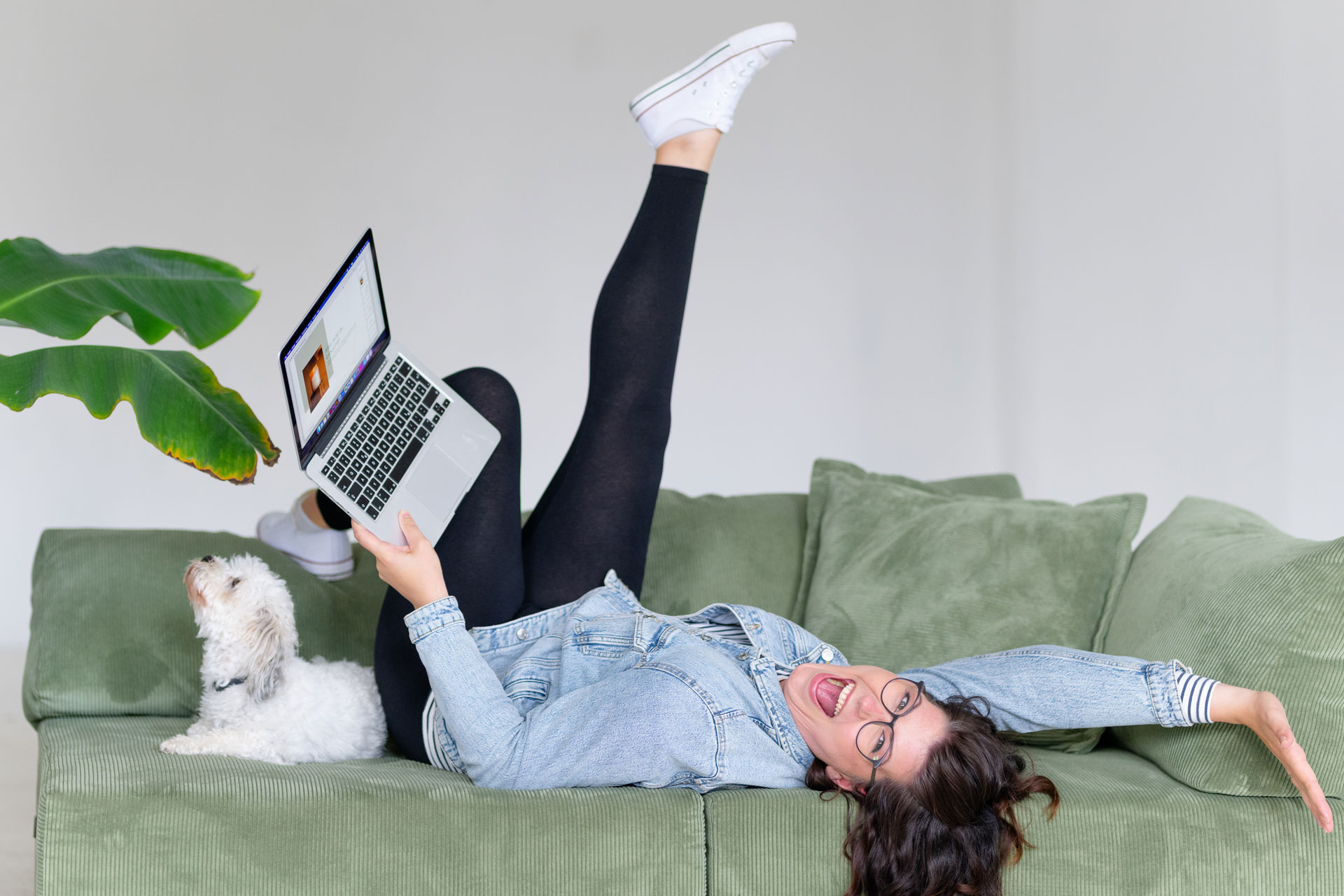 Evi liegt entspannt mit Laptop und Hund auf dem grünen Sofa