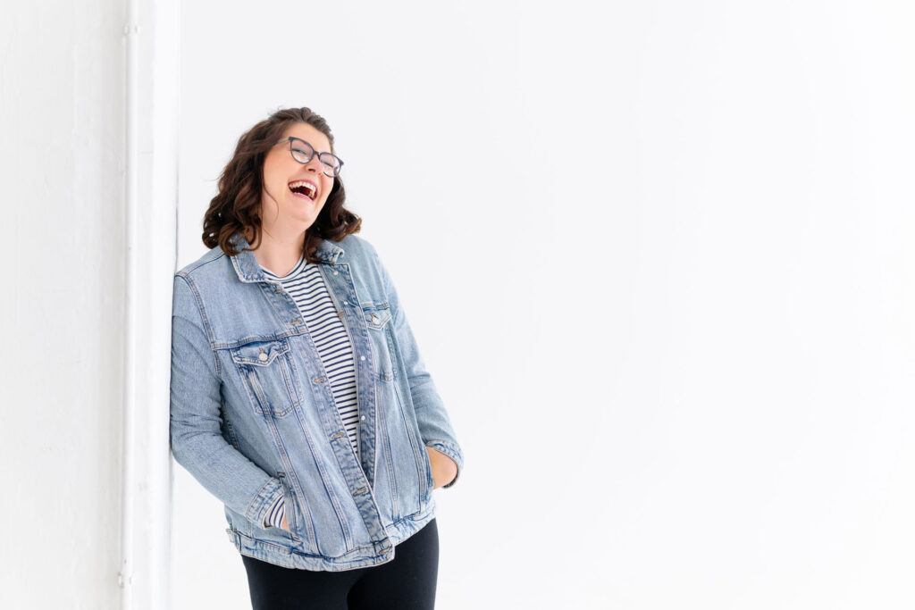 Evi in Jeansjacke lehnt lachend an einer Wand