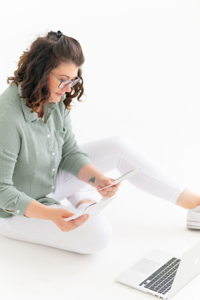 Evi sitzt im Schneidersitz auf dem Boden und schaut auf ein Tablet, daneben ein Laptop