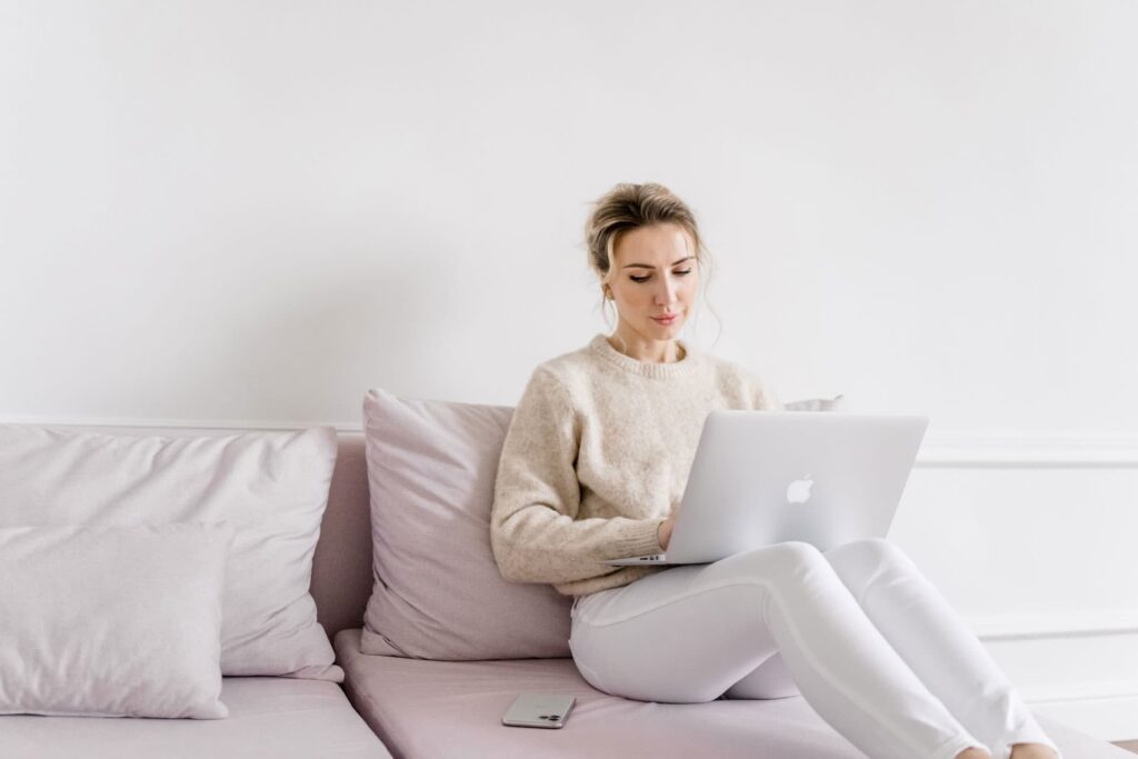 Fraue auf einem Rosa Sofa wie sie am Laptop einen Newsletter erstellt