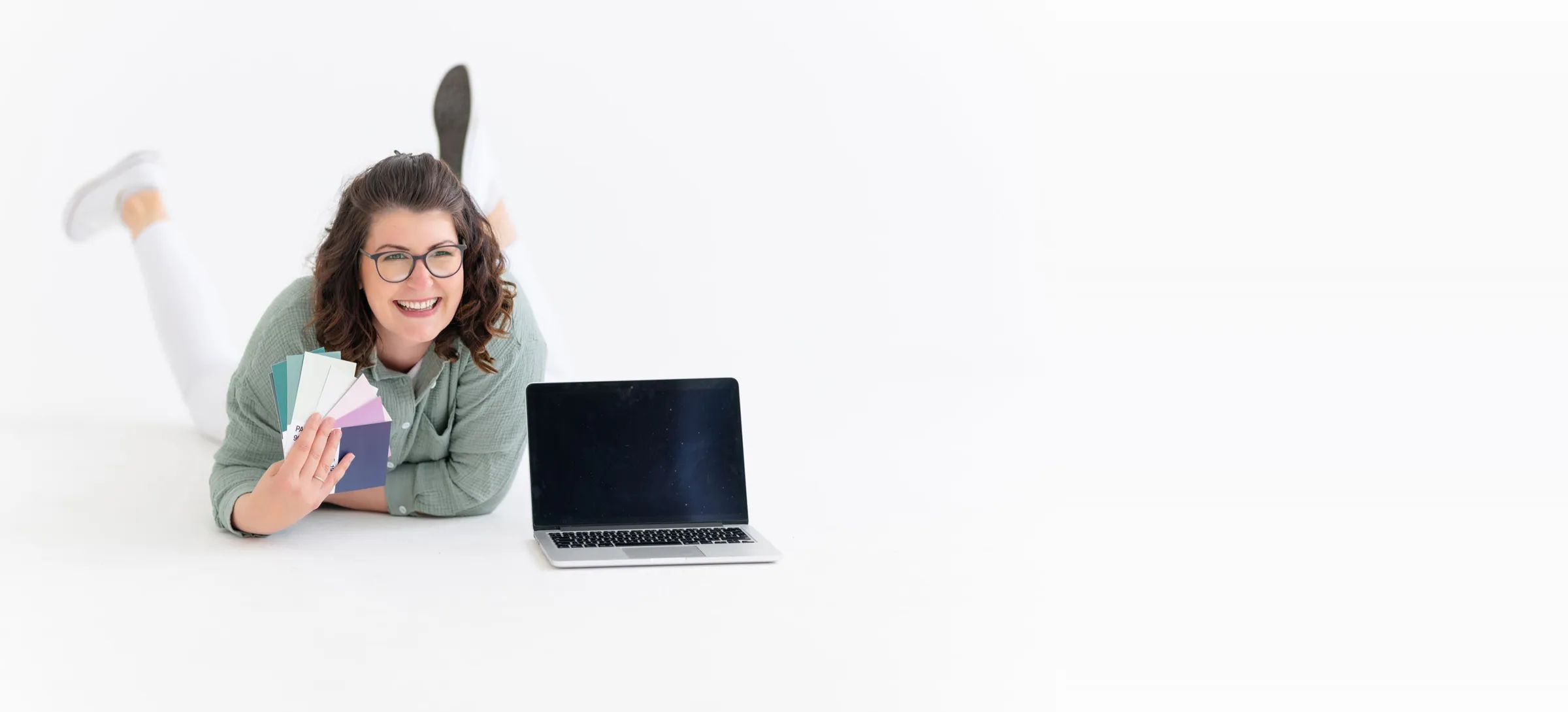 Evi Hollmann liegt lachend auf dem Boden, mit Farbfächer in der Hand und Laptop neben sich