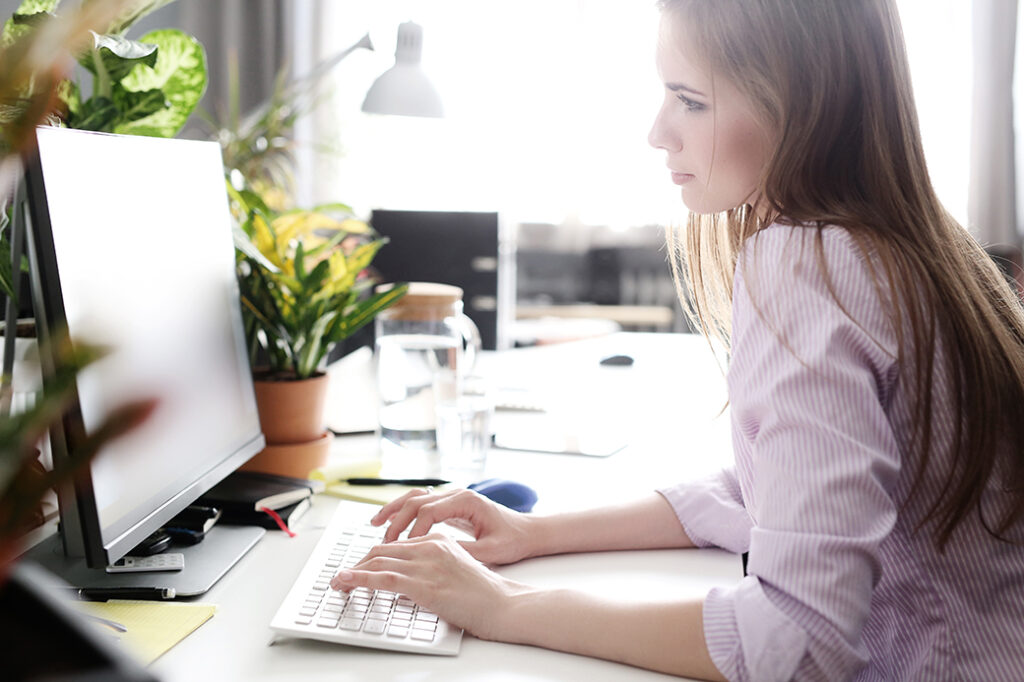 Frau arbeitet am Schreibtisch vorm Monitor auf der Suche nach dem perfekten WordPress Theme